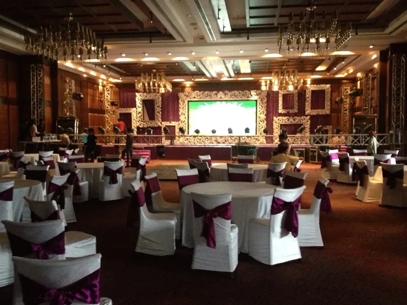A banquet hall of round tables in plum sashes facing an ornate white stage and LED wall