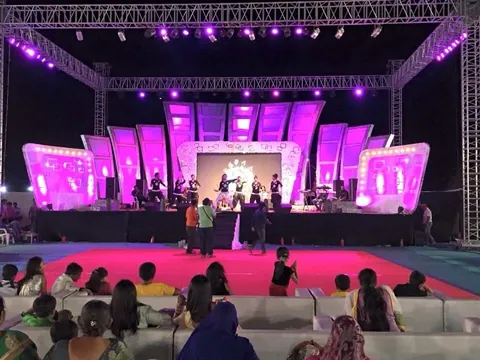 A large outdoor stage under truss lighting washed in magenta, with an audience watching a performance