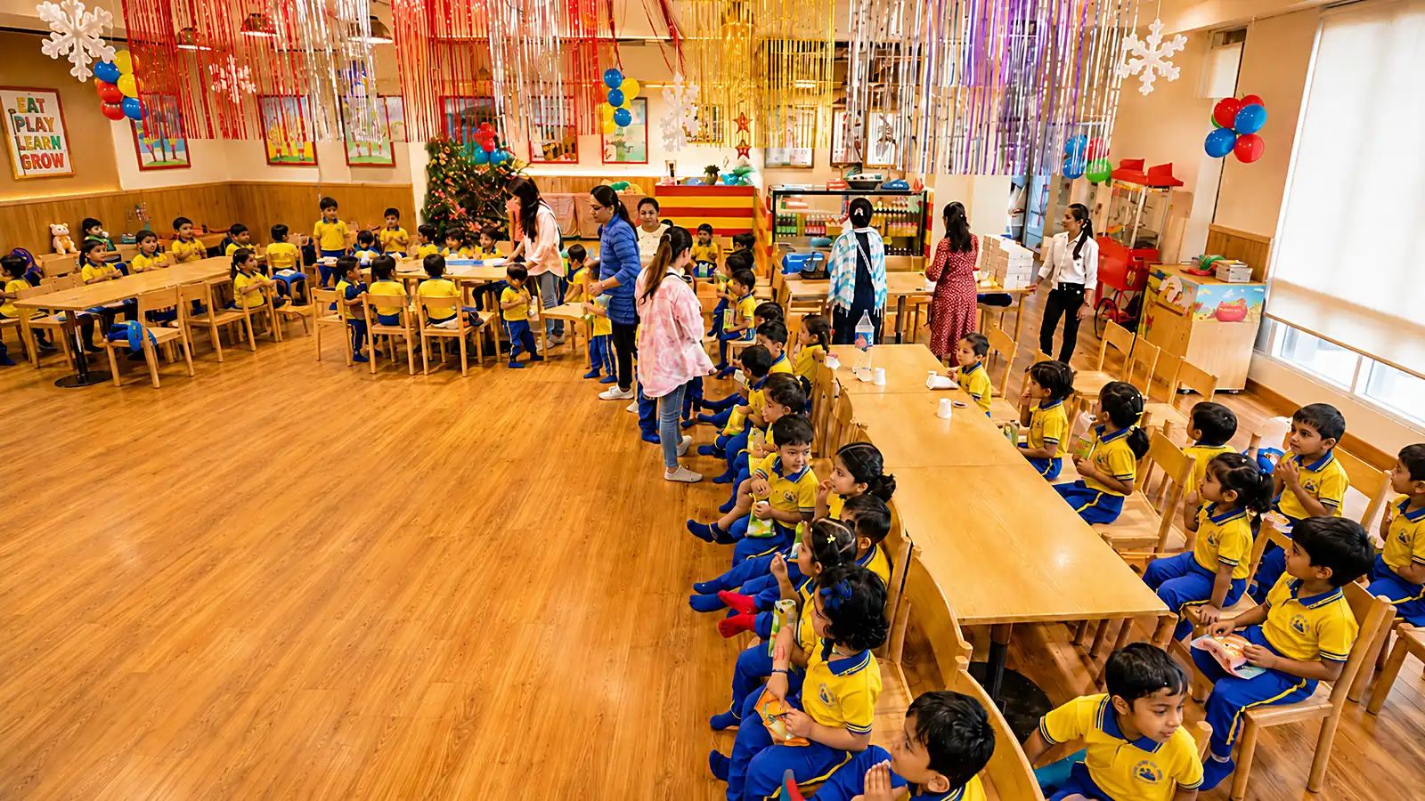 Children seated in rows at a school celebration, with streamers and a decorated backdrop behind them